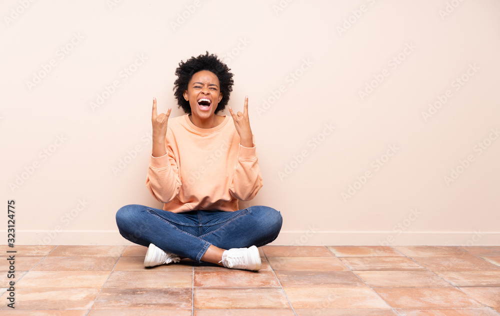 African american woman sitting on the floor making rock gesture