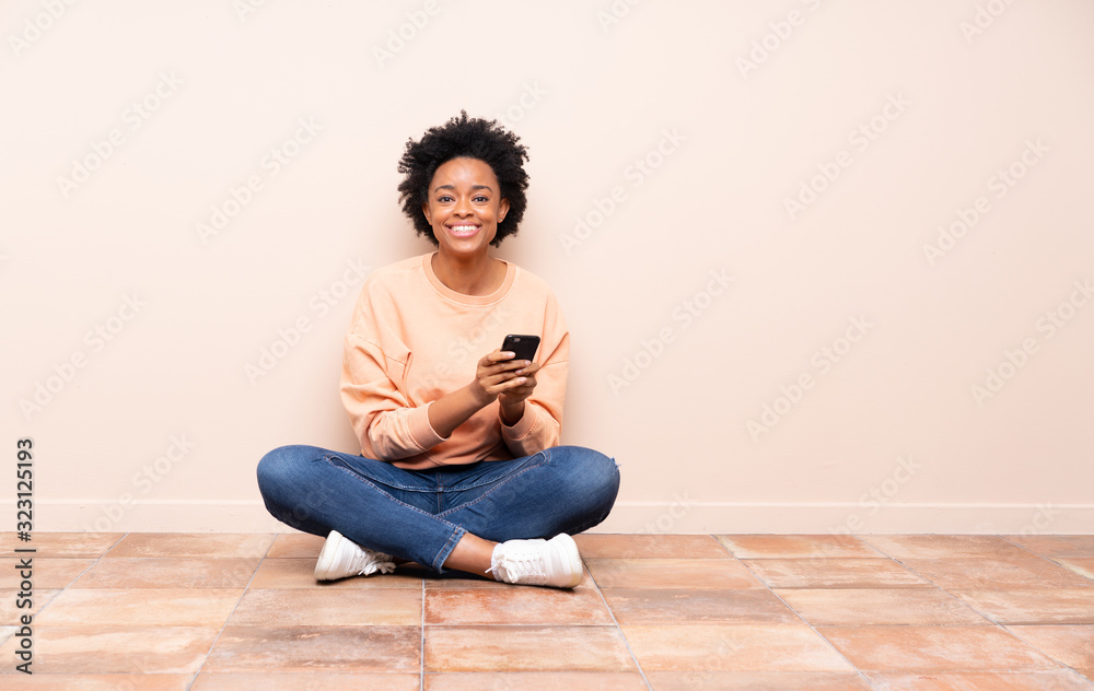 African american woman sitting on the floor sending a message with the mobile African american woman sitting on the floor sending a message with the mobile
