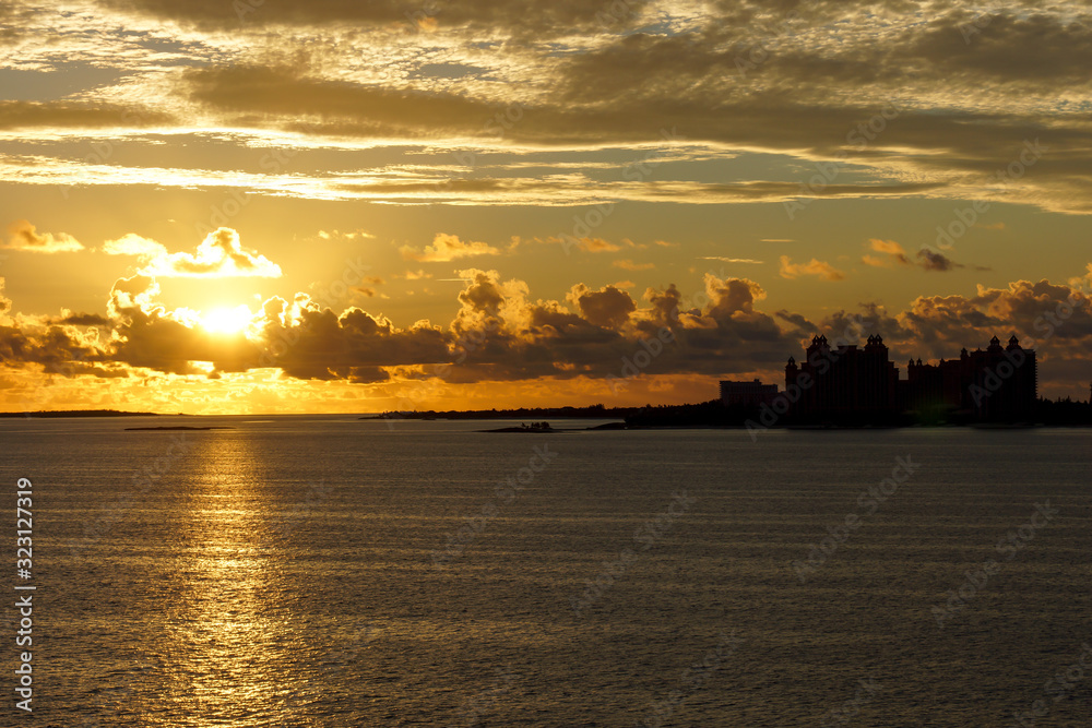 grateful sunrise over the ocean off the Bahama Islands with an orage sky, reflection on the sea and silhouettes of buildings in the background