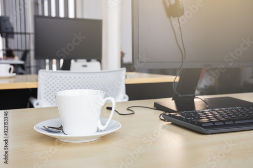 White coffee cup and personal computer on wooden table at office with light flare effect. 