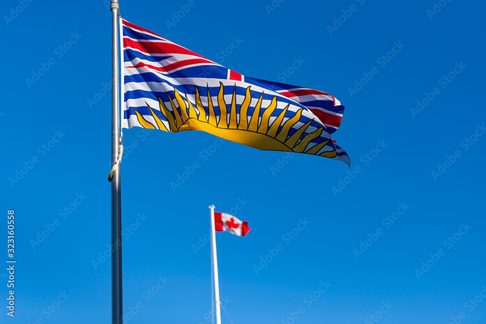 British Columbia flag flying with Canadian flag in background on a sunny day with blue sky  