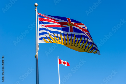 British Columbia flag flying with Canadian flag in background on a sunny day with blue sky  