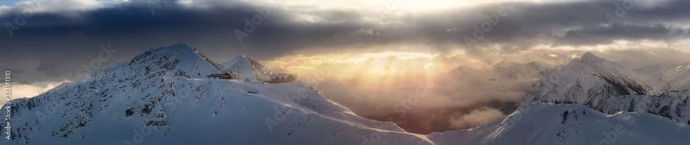 Fototapeta premium Kicking Horse, Golden, British Columbia, Canada. Beautiful Panoramic Aerial View of Canadian Mountain Landscape during a vibrant sunny and cloudy morning sunrise in winter. Chalet and Gondola