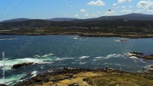 Sea birds flying over beautiful shoreline of Spanish coast with big cliffs splashed by white waves of blue sea, aerial view