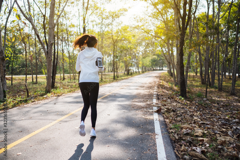 Fototapeta premium Rear view image of a young asian woman jogging in city park in the morning