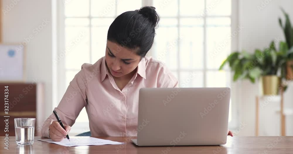 Serious indian businesswoman analyzing report using laptop in office Serious indian businesswoman analyzing report using laptop in office