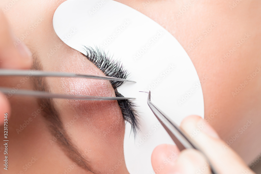 Naklejka premium Eyelash extension procedure. Master tweezers sets fake lashes on beautiful woman