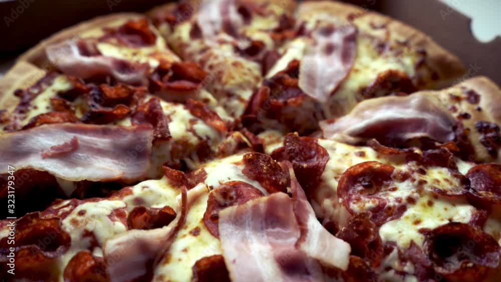 Closeup of american take away pizza. Dolly movement over delivered pizza. Fresh cheese, bacon and pepperoni. Unhealty eating concept. Closeup of american take away pizza. Dolly movement over delivered pizza. Fresh cheese, bacon and pepperoni. Unhealty eating concept.