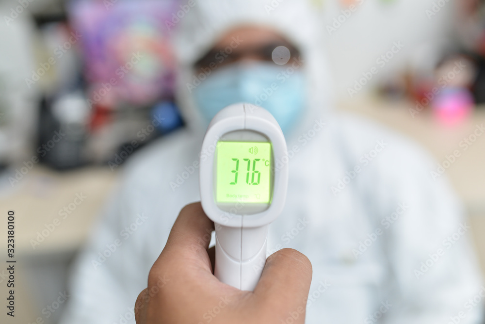 An Asian male doctor is measuring his body temperature with electronic thermometer before work to prevent the spread of the coronavirus outbreaks. The yellow color is warning temperature