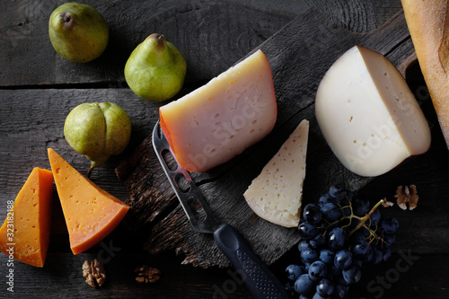 Homemade cheese slices assorted with green pears and black gape at dark background 