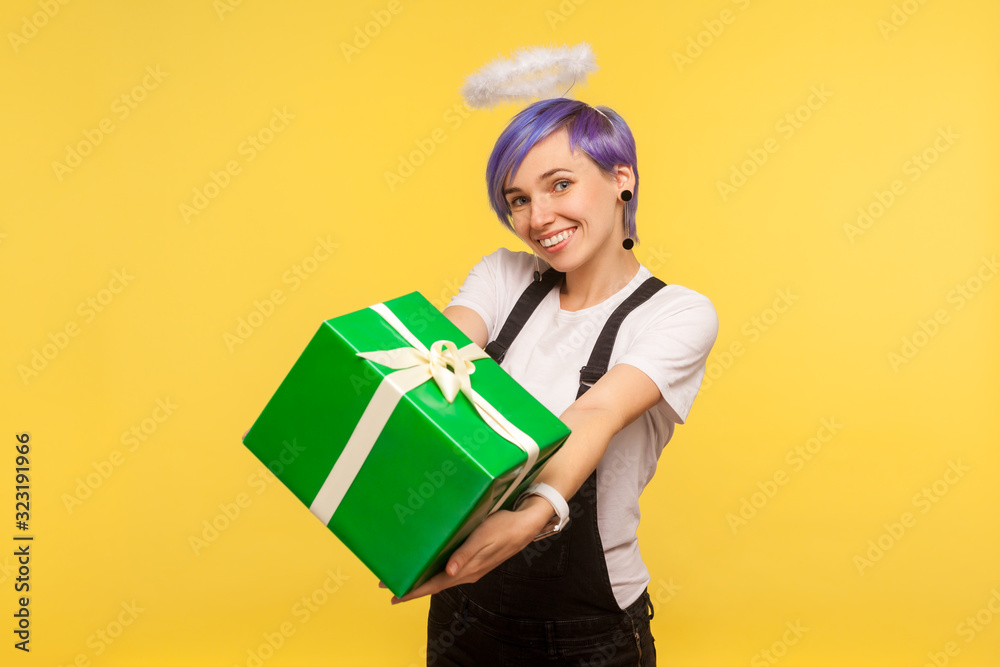 Portrait of charming joyful hipster girl with angelic halo over violet short hair giving wrapped present box to camera, congratulating and sharing gift. isolated on yellow background, studio shot Portrait of charming joyful hipster girl with angelic halo over violet short hair giving wrapped present box to camera, congratulating and sharing gift. isolated on yellow background, studio shot