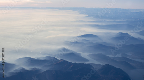Aerial view of the smog and fog that covers the Po Valley in Italy and the first mountains of the Alps. Landscape from airplane window. Pollution due to low rain and no wind