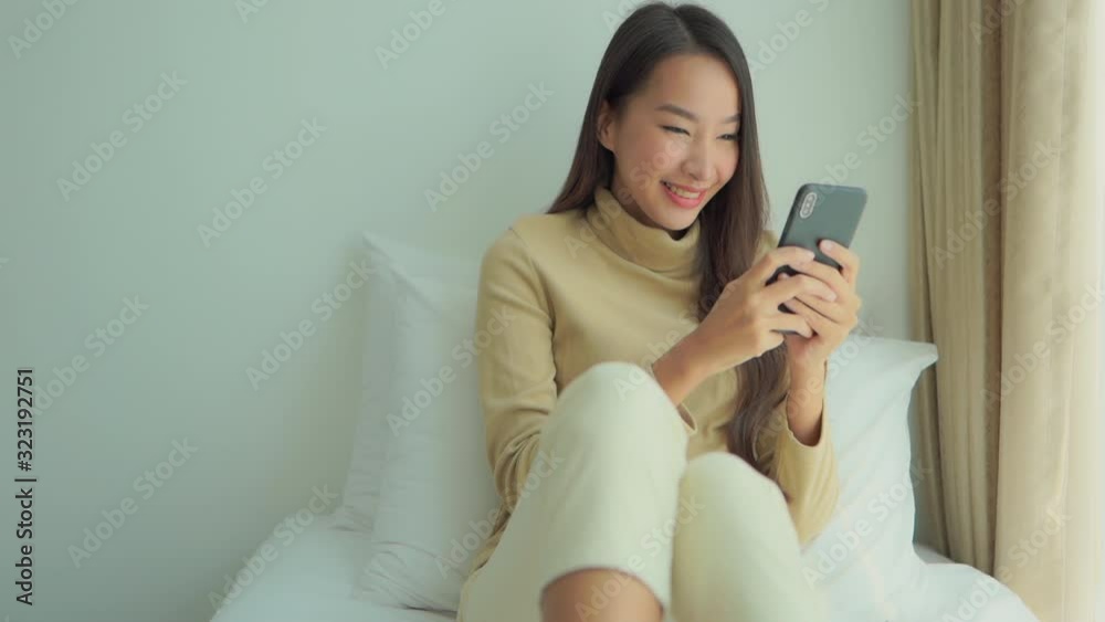 Smiling beautiful asian woman chatting on smartphone on bed Smiling beautiful asian woman chatting on smartphone on bed