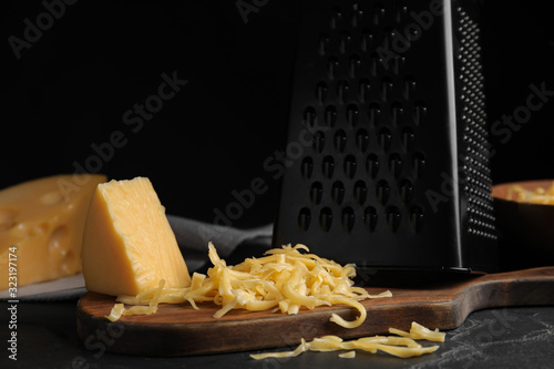 Delicious grated cheese on wooden board against black background photo