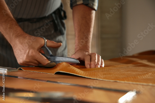 Man cutting leather with scissors in workshop, closeup