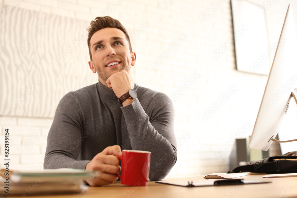 Young man with cup of drink relaxing at table in office during break Young man with cup of drink relaxing at table in office during break
