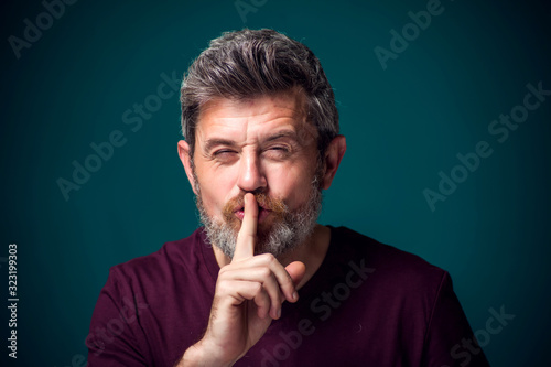 A portrait of bearded man showing hush gesture. People and emotions concept