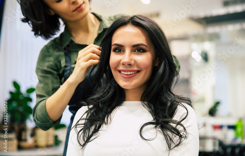 Work is done. Young happy woman in a white sweater is looking in the mirror, admiring her new hairstyle, made by a hairdresser in a beauty salon.