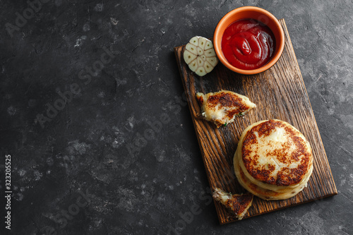 Potato pies with ketchup and garlic on a wooden Board. Dark concrete background, top view