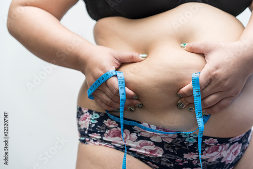 young woman used hands squeezing excess belly fat and cellulite of abdomen her dismayed near waist cause of fatty weight. concept of exercise, beauty or body firming gel, cream product or liposuction