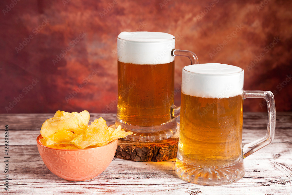 two beer mugs with foam and bowl of chips two beer mugs with foam and bowl of chips