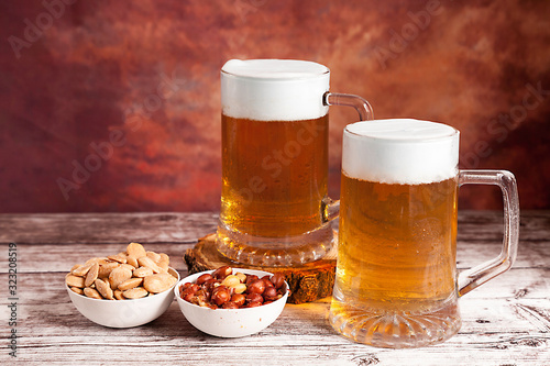 Two beer mugs with foam and bowls of peanuts and almonds
