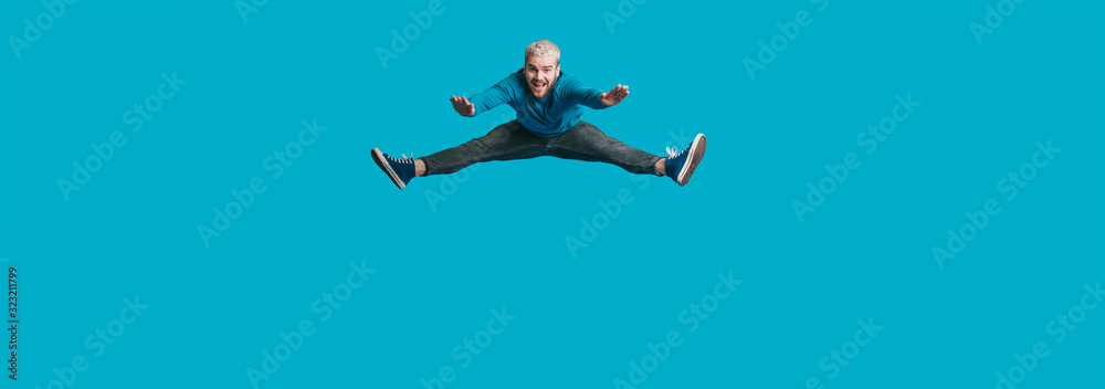 An excided man jumping and smiling on a blue blank space imitating as if he was pushed by something