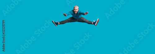 An excided man jumping and smiling on a blue blank space imitating as if he was pushed by something