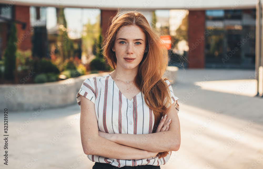 A nice picture of a gorgeous red haired woman looking confident and posing outside in front of a big company A nice picture of a gorgeous red haired woman looking confident and posing outside in front of a big company