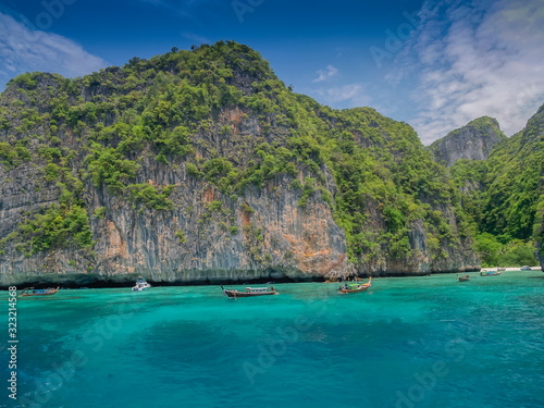 Sea view of long-tail boat running in blue-green sea with rock cliff mountain and blue sky background, Peacock island, Loh Samah Bay, Phi Phi islands, Krabi, southern of Thailand.