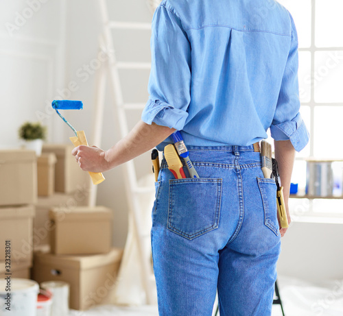 Pretty woman painting interior wall of home with paint roller