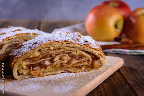 Delicious strudel stuffed with apples and cinnamon and red apples on background