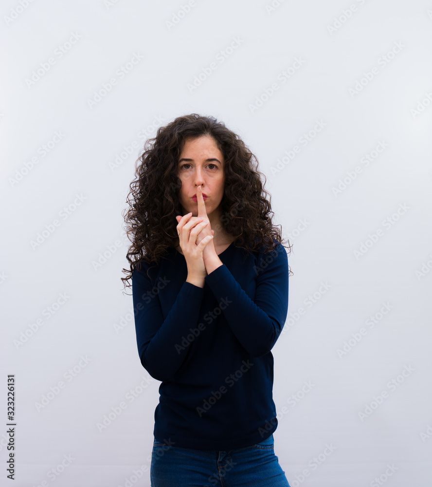 young pretty woman with black curly hair looking serious and cross with finger pressed to lips demanding silence or quiet, keeping a secret. young pretty woman with black curly hair looking serious and cross with finger pressed to lips demanding silence or quiet, keeping a secret.