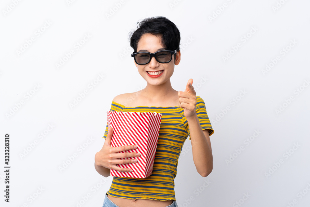 Young Asian girl with 3d glasses and holding a big bucket of popcorns while pointing front Young Asian girl with 3d glasses and holding a big bucket of popcorns while pointing front