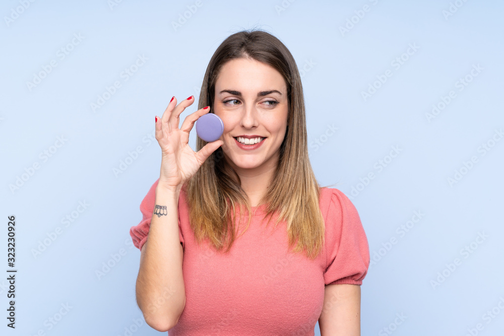 Young blonde woman over isolated blue background holding colorful French macarons Young blonde woman over isolated blue background holding colorful French macarons