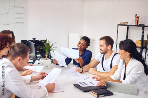 Creation of new business idea by multiethnic group sitting in meeting office  white interior background. Wearing formal wear  holding papers. Asian  caucasian  african partnership