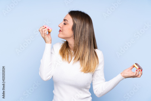 Young blonde woman over isolated blue background holding donuts with happy expression