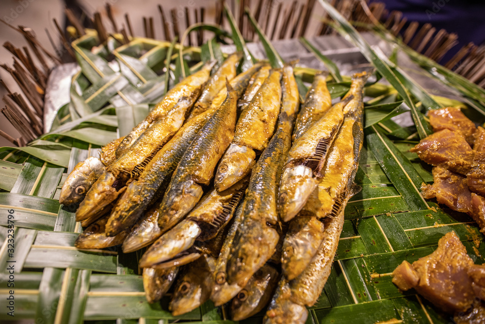 Grilled fish on skewers served on green palm leaves top view in close-up from above with copy space