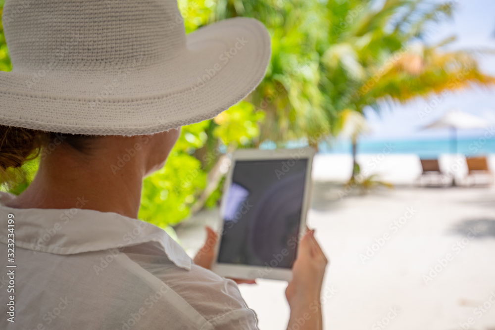 Tropical beach and woman relaxing with blank tablet sitting on the sun chair