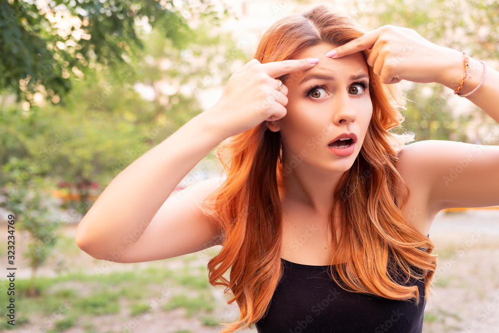 Beautiful plus size woman squeezing pimple on her forehead using her hands. Summer outdoor portrait, copy space