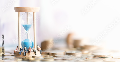 Miniature people: Elderly people sitting on hourglass with coins stack. social security income and pensions. Money saving and Investment. Time counting down for retirement concept.