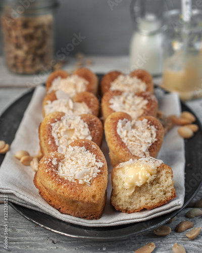 food photography of homemade sponge biscuit cakes filled with cream covered with coconut flakes close up on a dark metal dish on a gray texture background