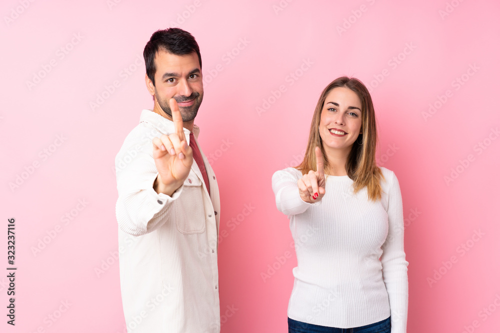 Couple in Valentine Day over isolated pink background showing and lifting a finger Couple in Valentine Day over isolated pink background showing and lifting a finger
