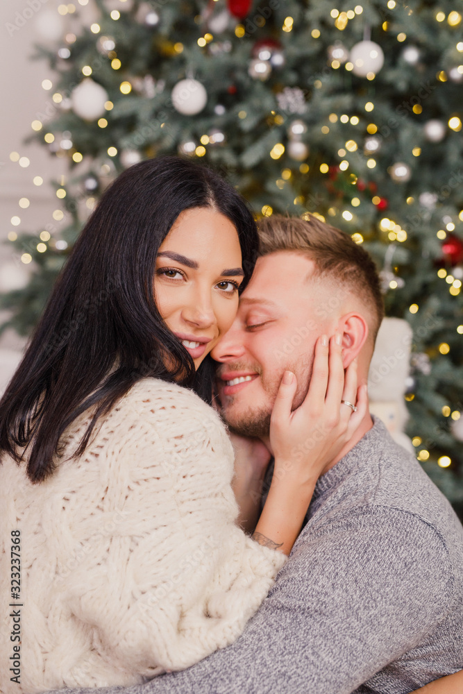 young beautiful couple, brunette girl in a white sweater, a blond man in a gray sweater sitting near a Christmas tree young beautiful couple, brunette girl in a white sweater, a blond man in a gray sweater sitting near a Christmas tree
