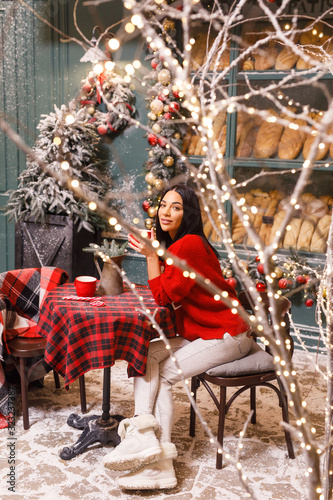 young beautiful brunette girl in a red sweater and white pants drinks tea on a street in Paris against the background of a window of a bread shop