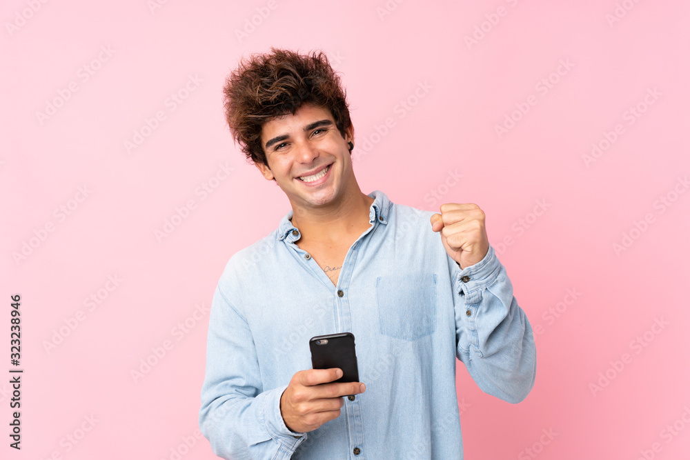 Young caucasian man with jean shirt over isolated pink background with phone in victory position Young caucasian man with jean shirt over isolated pink background with phone in victory position