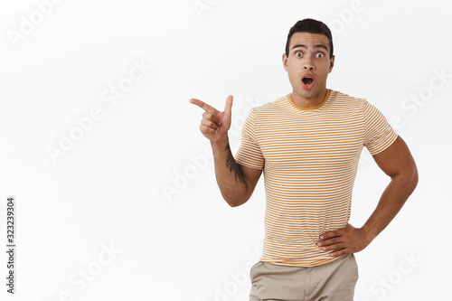 Can you believe it, look. Impressed, speechless handsome young masculine man, athlete pointing fingers left, inviting go sportclub together, found perfect offer, white background