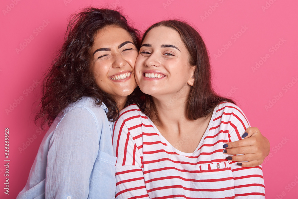 Close up portrait of two attractive caucasian smiling women iposing solated on over pink studio background, brunettef emales hugging each other andlooking directly at camera. Friendship concept. Close up portrait of two attractive caucasian smiling women iposing solated on over pink studio background, brunettef emales hugging each other andlooking directly at camera. Friendship concept.
