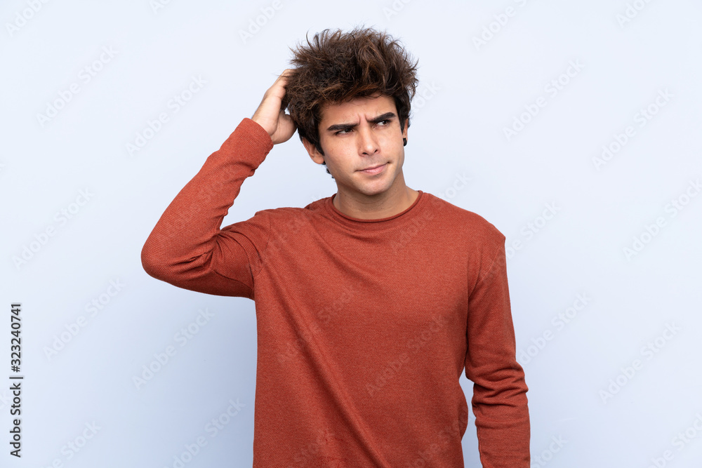 Young caucasian man over isolated blue background having doubts while scratching head Young caucasian man over isolated blue background having doubts while scratching head
