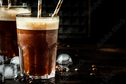 Cold frappe coffee with ice and foam in large glasses on brown background, selective focus